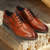 Men's Bugatti derby cognac leather shoes with a round toe and plain toe featuring a stacked heel , a tpr outsole , and laces fastening.