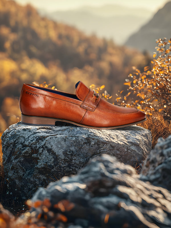 A cognac Men's bugatti Bit Loafer featuring a round toe apron toe, moulded  heel. Made from premium genuine leather with a durable high quality synthetic outsole, this slip-on design offers both style and comfort.