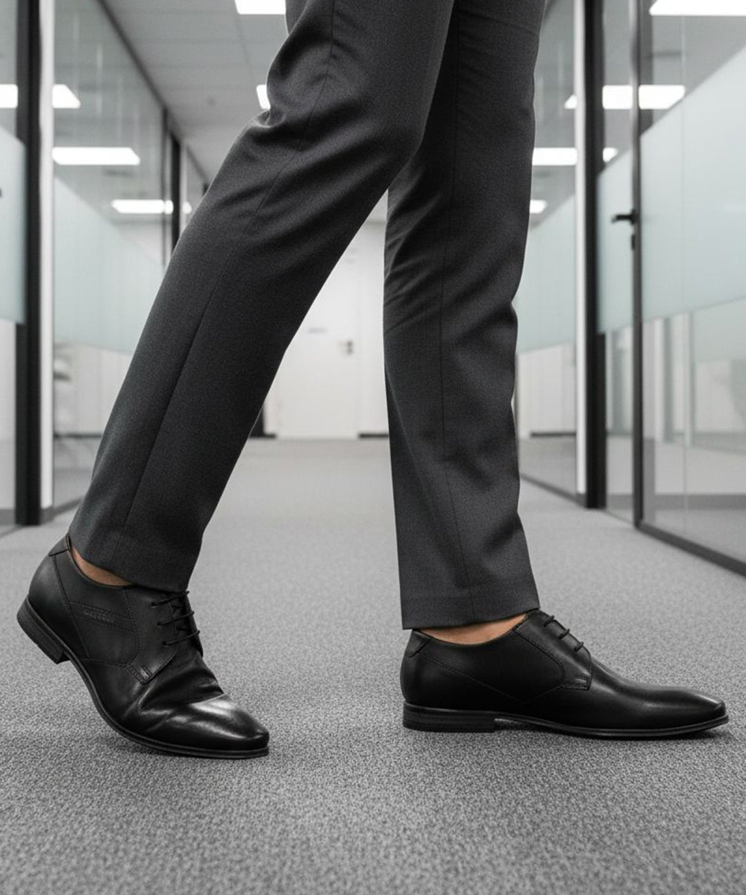 bugatti Morino I black leather derby shoes, paired with grey dress pants, in an office hallway.
