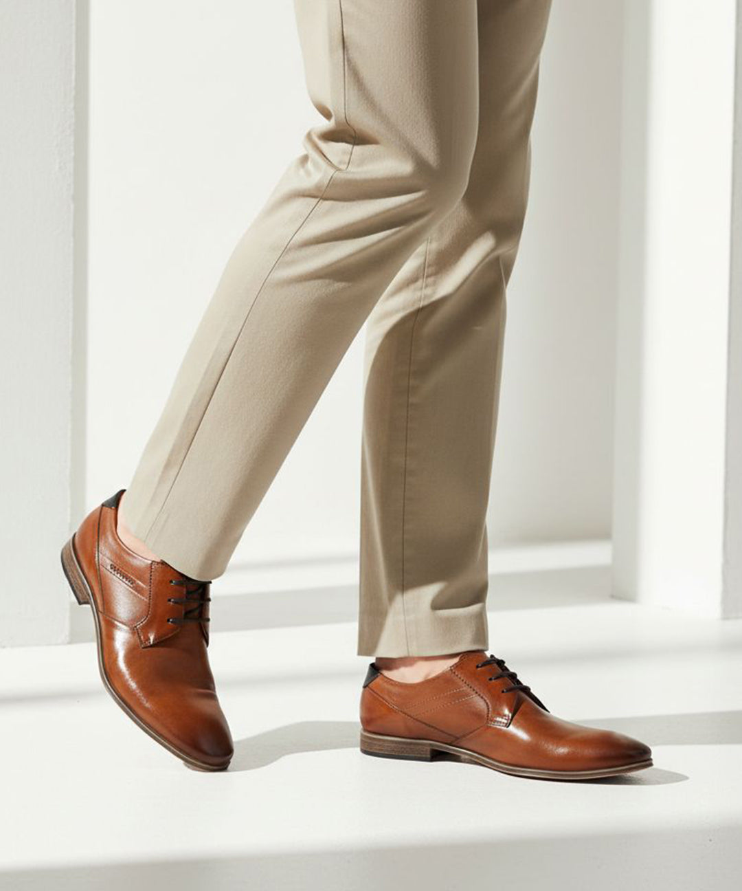 bugatti Morino I cognac brown leather formal shoes with black laces, styled with tan slacks.
