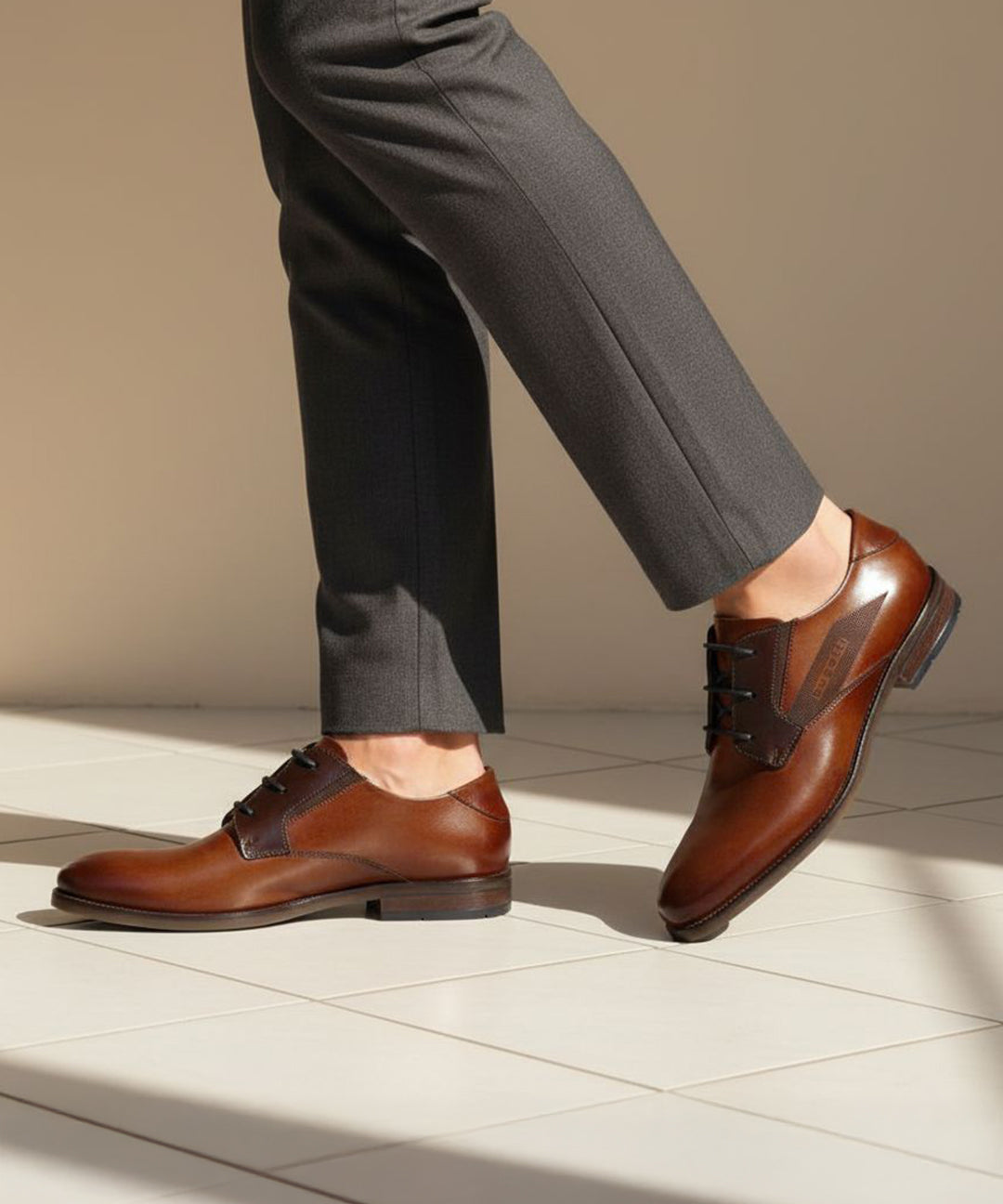 bugatti Sula cognac leather derby shoes, paired with gray dress pants, on a tiled surface.
