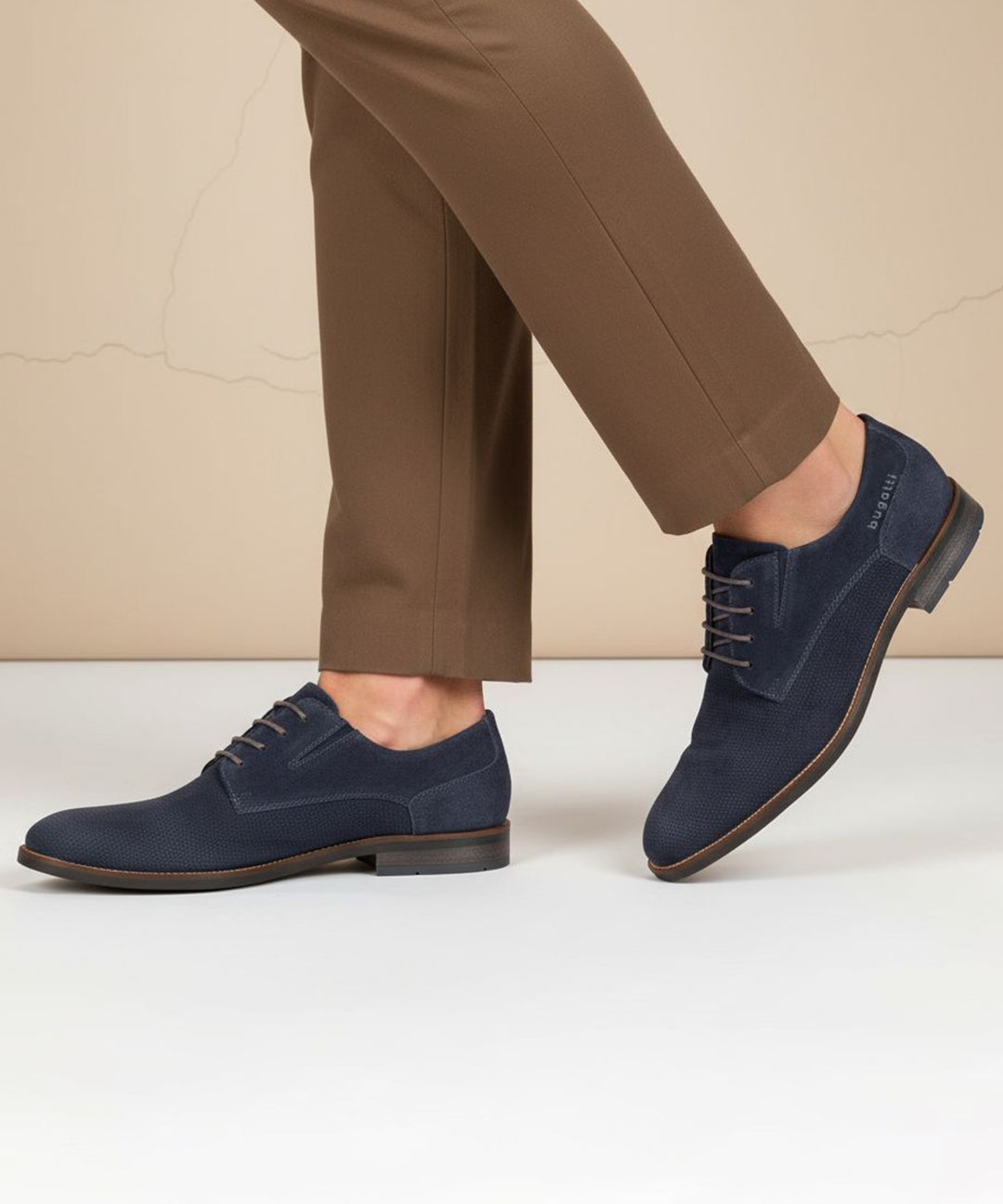 Lifestyle image of bugatti Sula dark blue leather derby shoes with brown laces, worn with brown trousers.