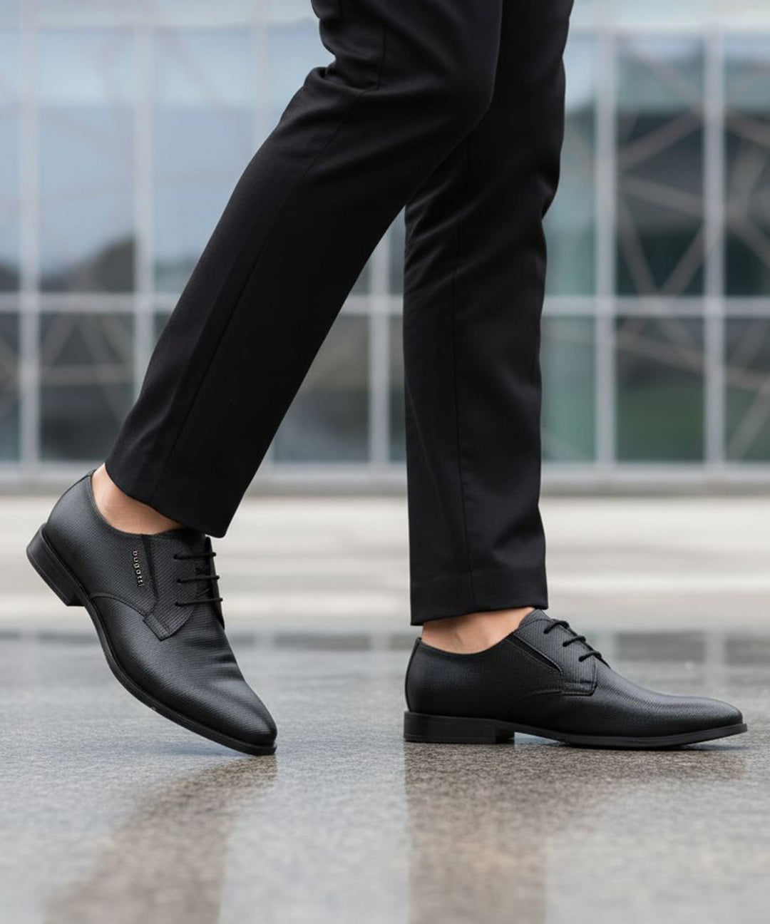 Cropped lifestyle shot of bugatti black leather formal derby shoes with textured design, paired with black dress pants.
