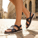 bugatti Limon dark blue leather sandals with criss-cross straps and a back strap on a cobblestone street.
