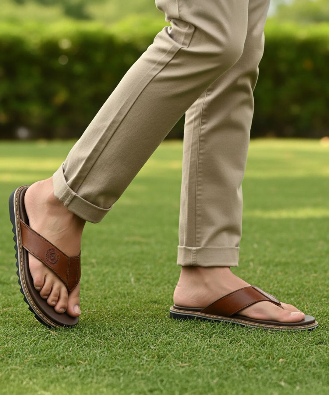 bugatti Limon cognac leather thong sandals, with a black ridged sole, worn with khaki trousers on grass.

