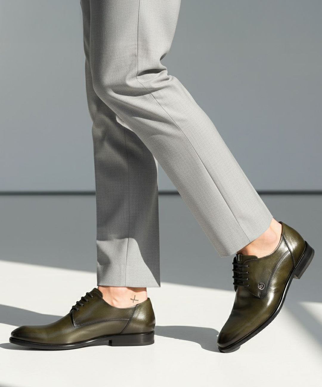 bugatti Mansueto Flex Derby shoes in dark green premium leather, worn with grey dress pants and a small ankle tattoo.
