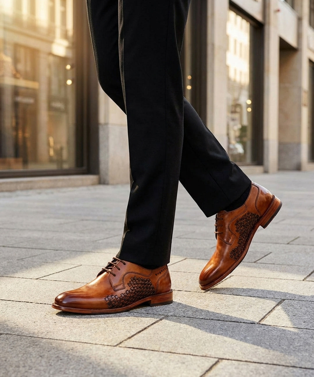 Lifestyle view of bugatti Livorno Flex Evo cognac leather derby shoes with a woven pattern, paired with black dress pants.
