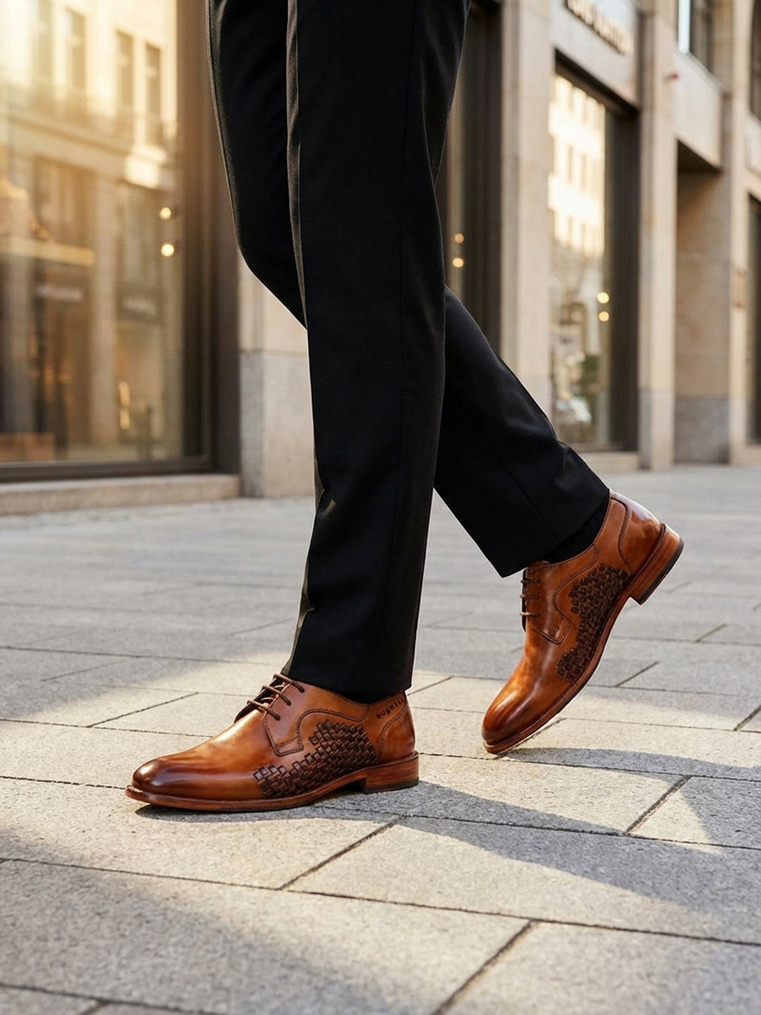 Lifestyle view of bugatti Livorno Flex Evo cognac leather derby shoes with a woven pattern, paired with black dress pants.
