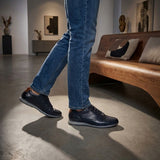 Lifestyle view of bugatti Thorello dark blue leather sneakers with blue jeans and casual indoor setting.
