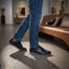 Lifestyle view of bugatti Thorello dark blue leather sneakers with blue jeans and casual indoor setting.
