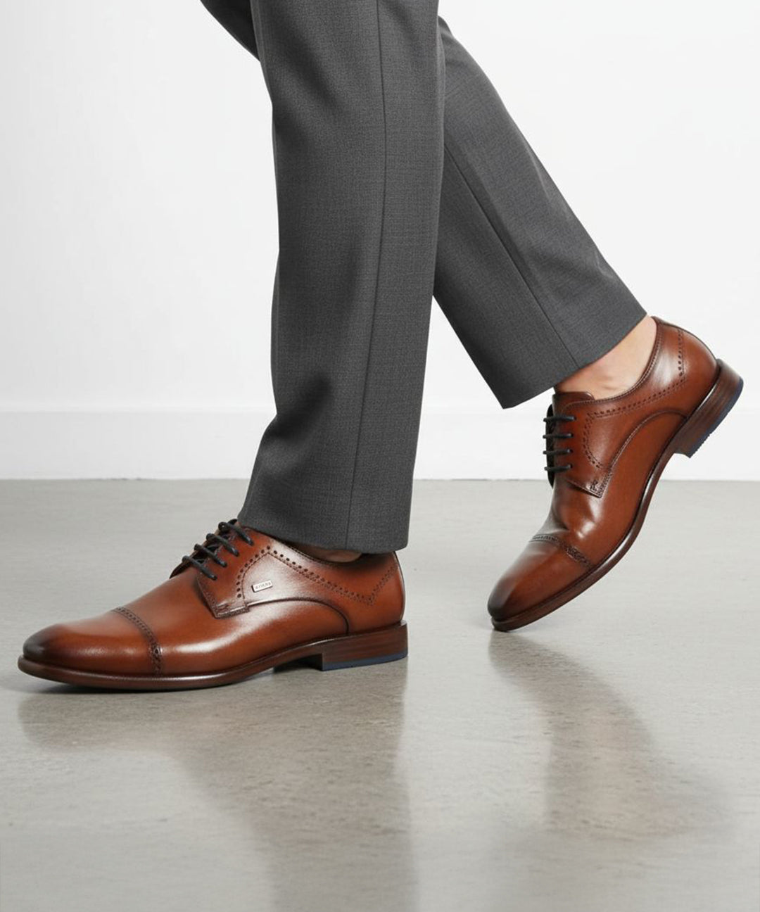 Lifestyle shot of bugatti Mansueto Flex Cognac leather derby formal shoes with black laces and blue sole accent.
