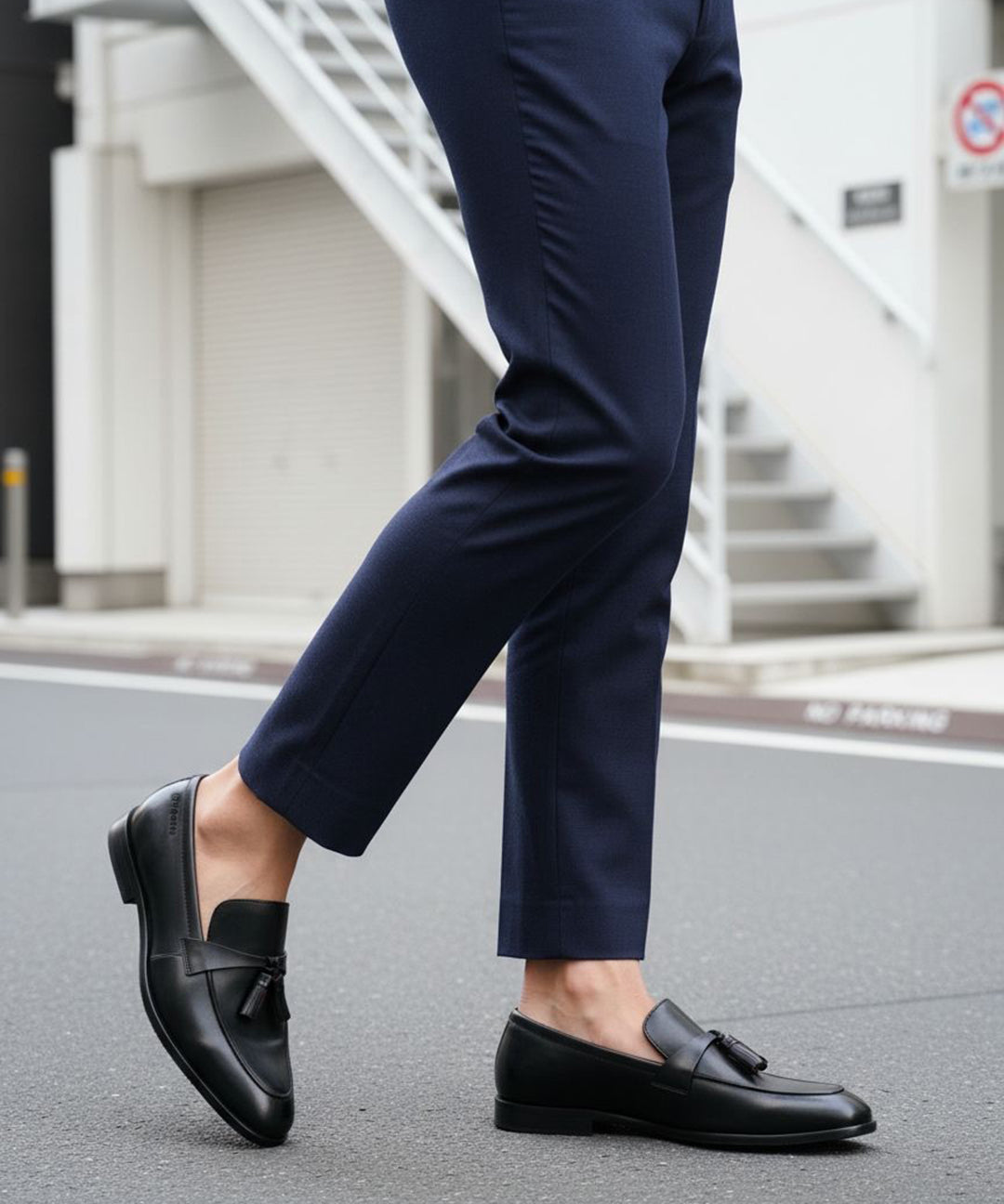 Cropped view of bugatti Rico black leather slip-on dress shoes with tassels, worn with navy trousers.

