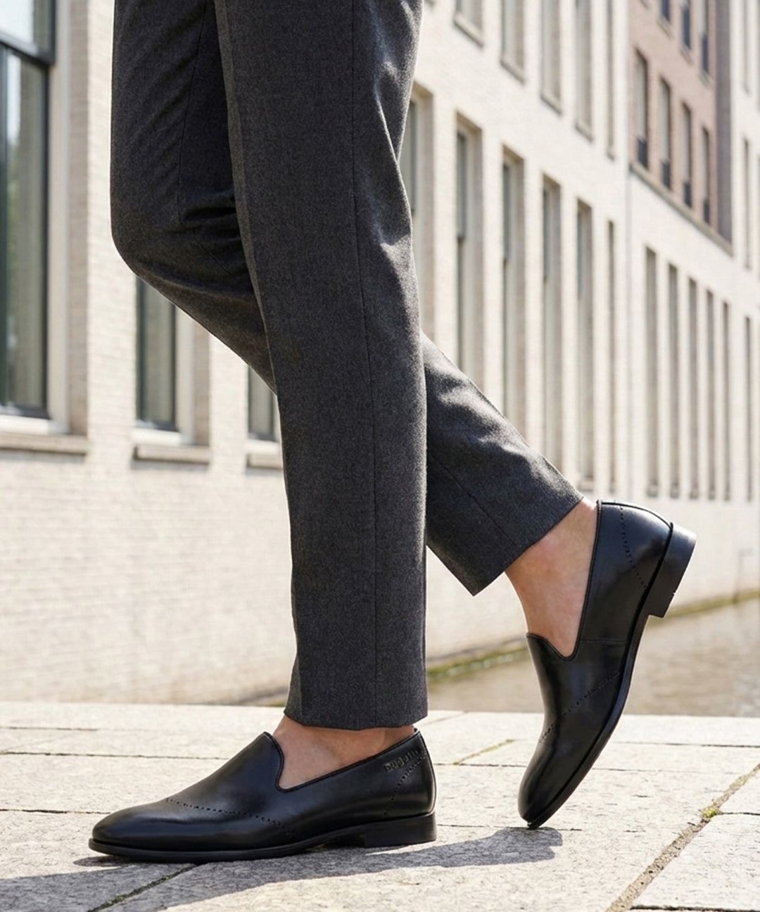 Cropped lifestyle shot of bugatti Rico black leather slip-on formal shoes, paired with gray dress pants.
