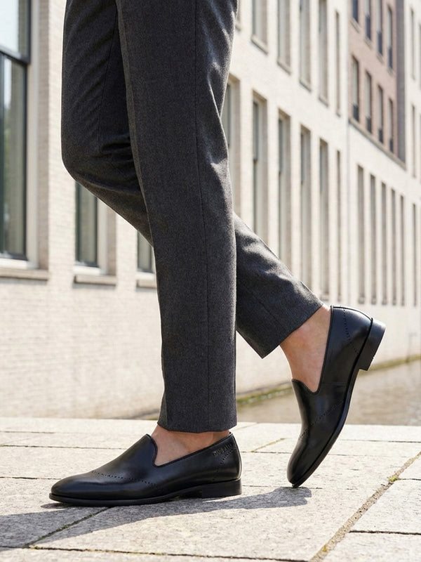 Cropped lifestyle shot of bugatti Rico black leather slip-on formal shoes, paired with gray dress pants.
