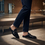 Lifestyle shot of bugatti Rico Black leather slip-on shoes, featuring a metal buckle detail.
