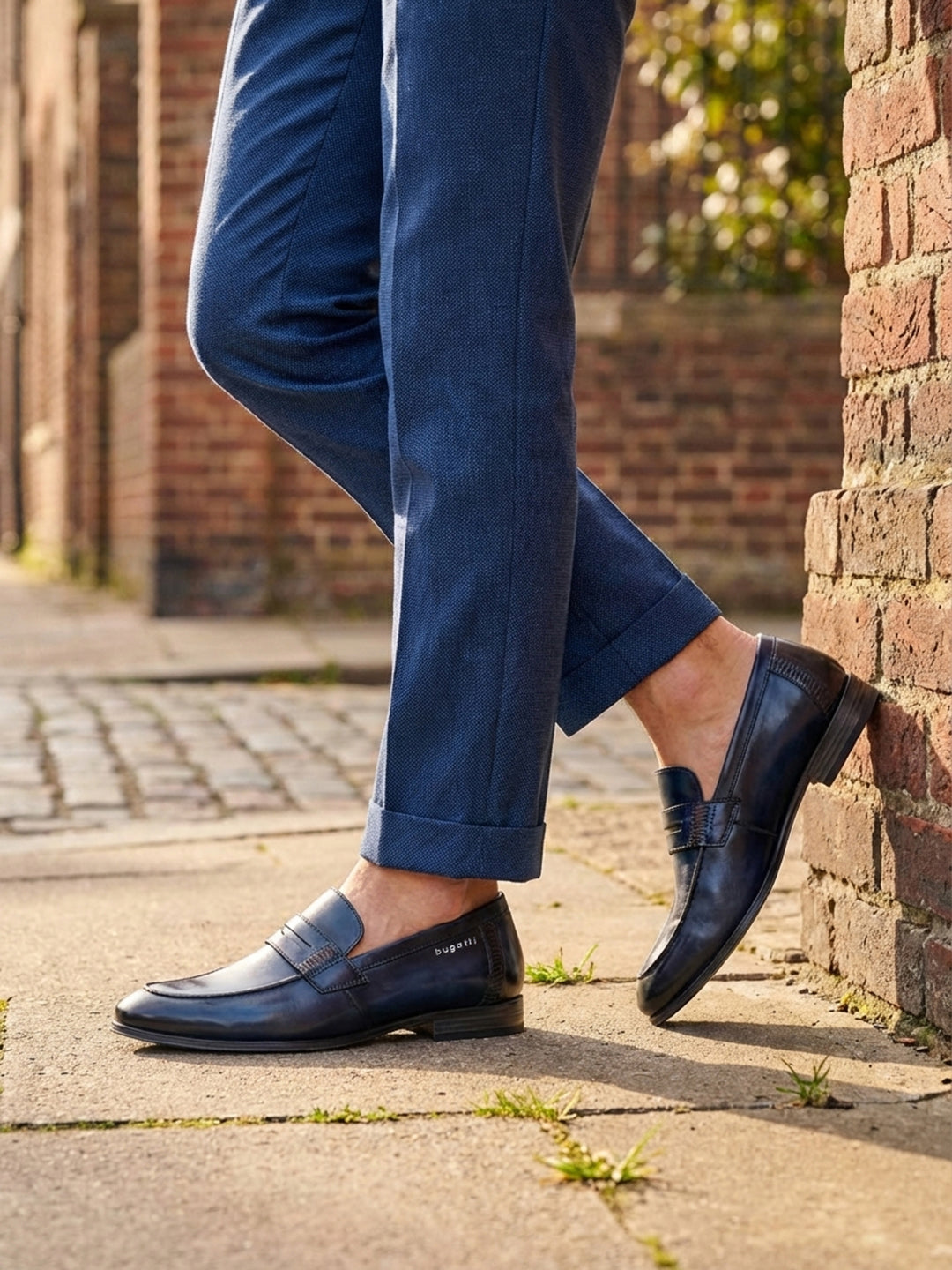 bugatti Matina blue leather penny loafers with a dark finish, worn with blue textured dress pants.