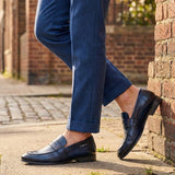 bugatti Matina blue leather penny loafers with a dark finish, worn with blue textured dress pants.