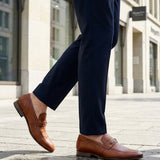 Cropped lifestyle image showing bugatti Matina cognac leather slip-on formal shoes with dark trousers.
