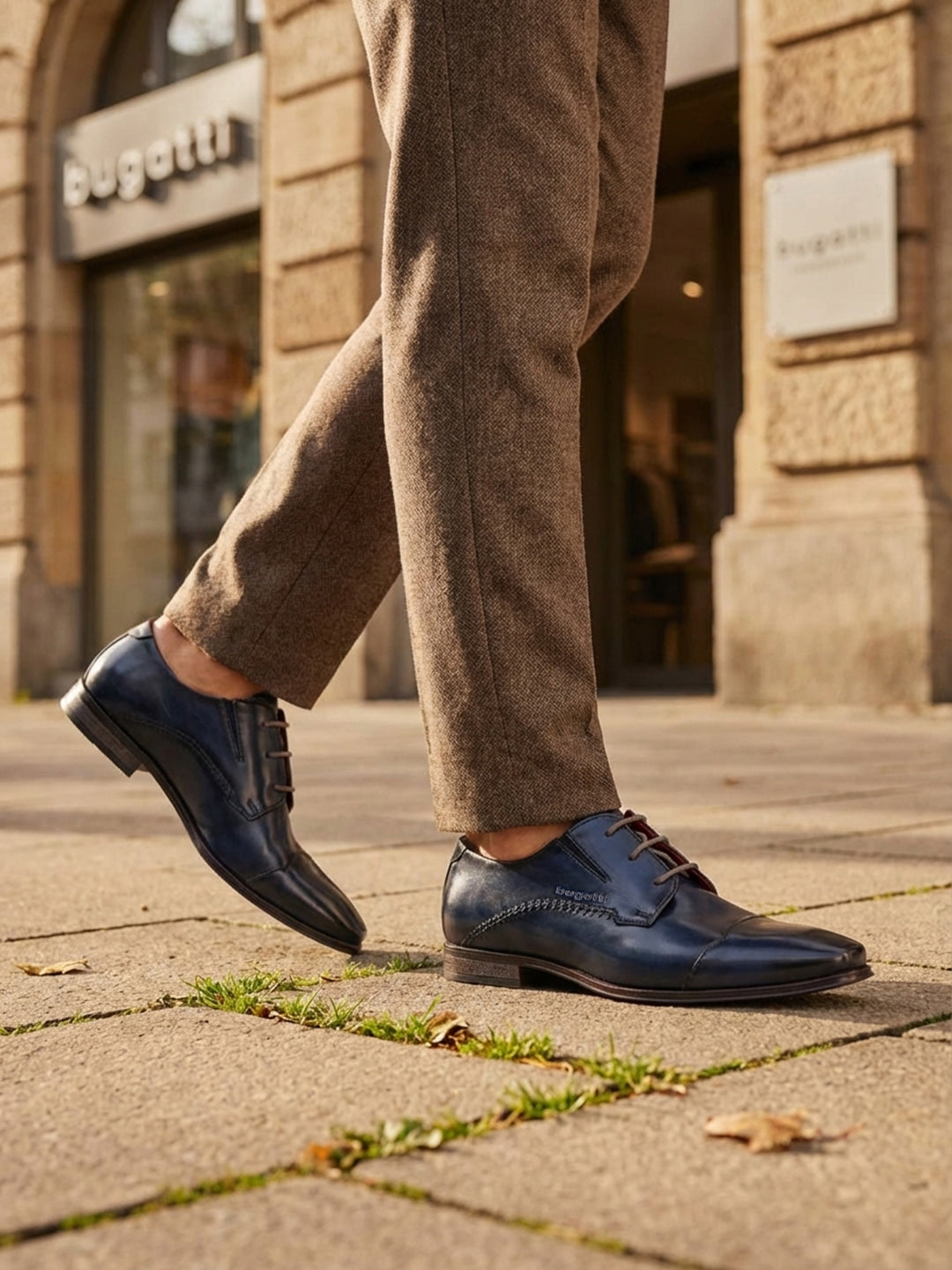Lifestyle shot of bugatti Margo blue leather derby shoes with brown laces and textured upper, paired with brown tweed trousers.
