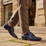 Lifestyle shot of bugatti Margo blue leather derby shoes with brown laces and textured upper, paired with brown tweed trousers.
