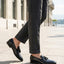 bugatti Margo black leather slip-on shoe with tassel detail, paired with gray trousers.

