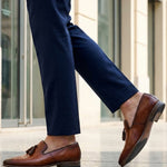 bugatti Margo cognac leather slip-on shoes with tassels, worn with dark blue pants in a lifestyle shot.
