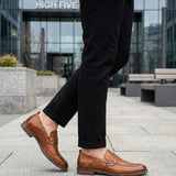 bugatti Sula Revo cognac penny loafers in premium leather, paired with black textured pants, outdoor setting.

