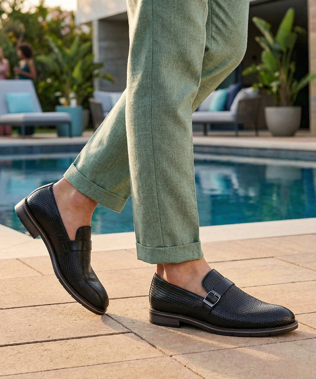 bugatti Laziano black leather loafers with a buckle, worn with green pants near a pool.
