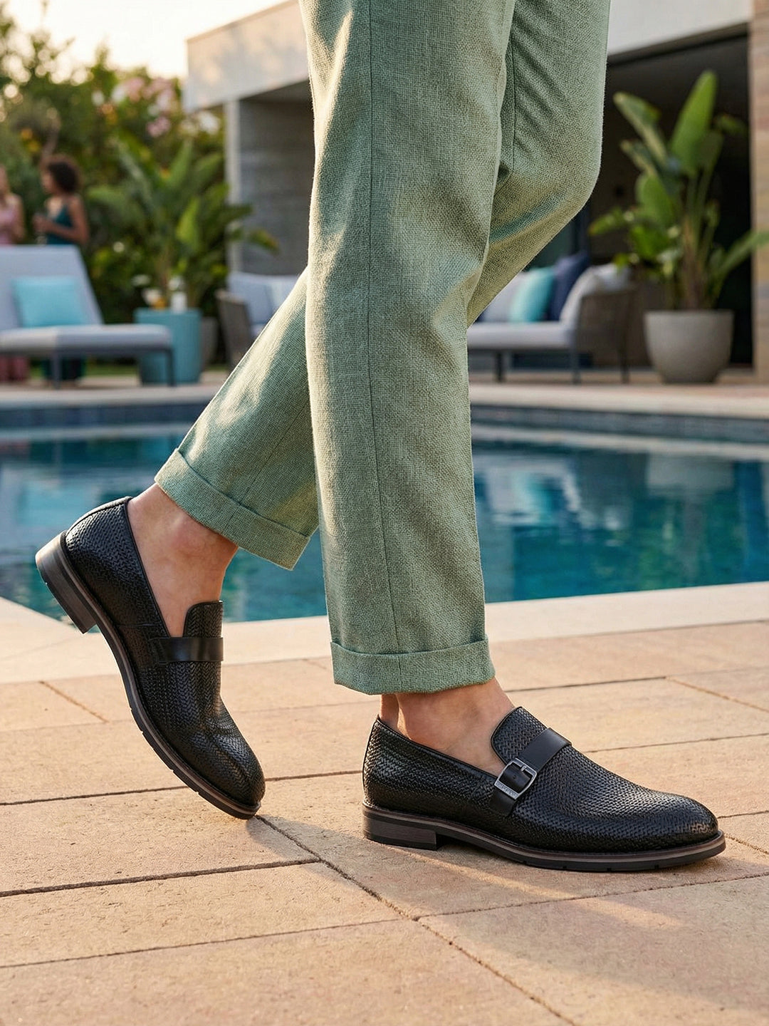 bugatti Laziano black leather loafers with a buckle, worn with green pants near a pool.
