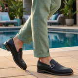 bugatti Laziano black leather loafers with a buckle, worn with green pants near a pool.
