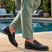 bugatti Laziano black leather loafers with a buckle, worn with green pants near a pool.
