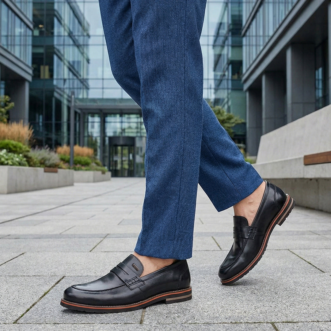 bugatti Caleo black leather penny loafers with brown trim worn with blue trousers.
