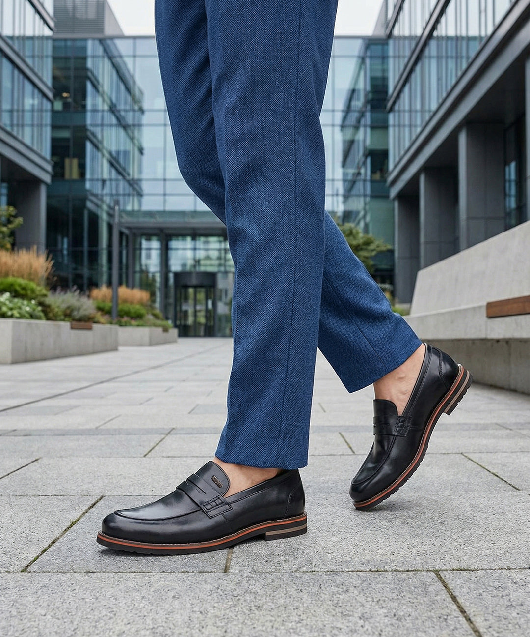bugatti Caleo black leather penny loafers with brown trim worn with blue trousers.
