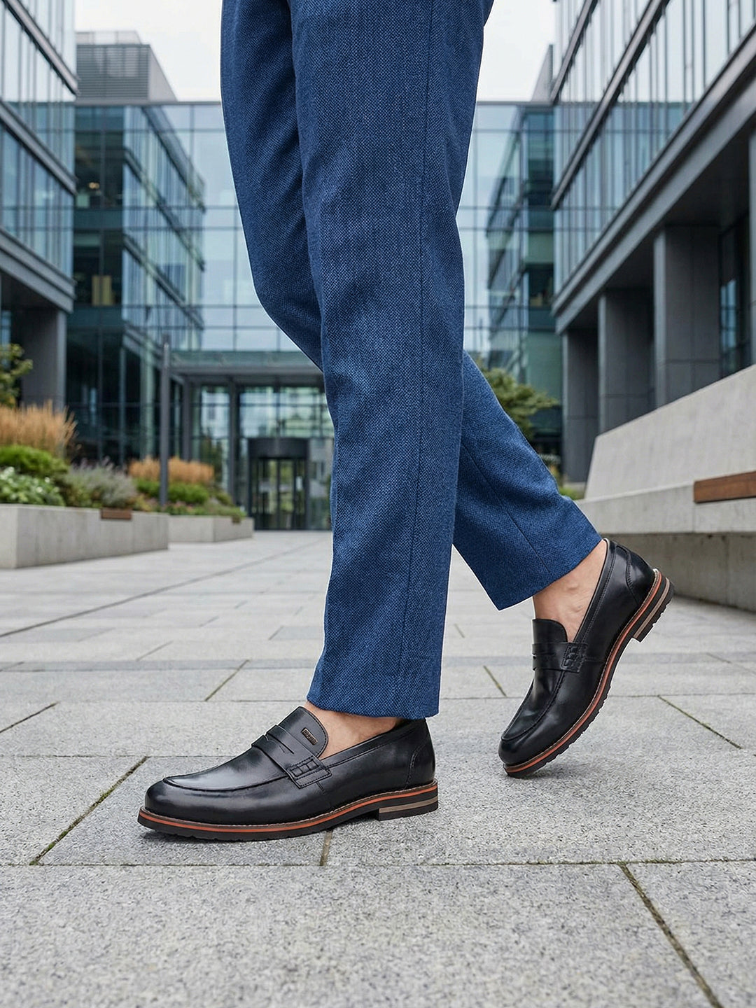 bugatti Caleo black leather penny loafers with brown trim worn with blue trousers.
