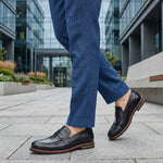 bugatti Caleo black leather penny loafers with brown trim worn with blue trousers.

