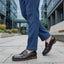 bugatti Caleo black leather penny loafers with brown trim worn with blue trousers.
