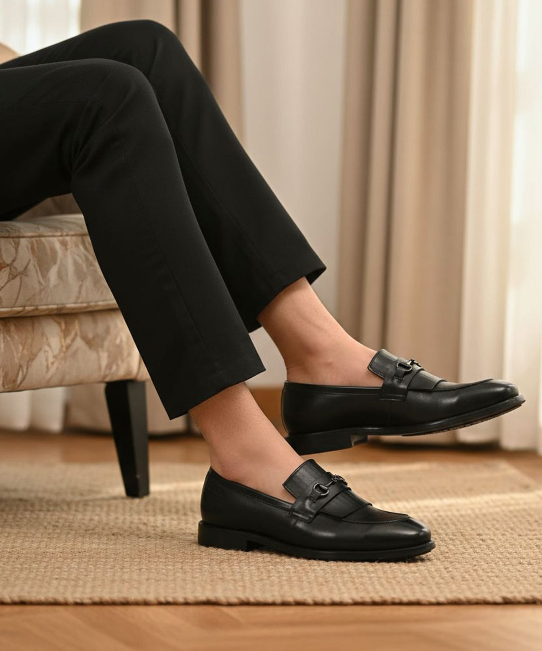 Lifestyle shot of black bugatti leather slip-on dress shoes, worn with black pants, and displayed on a rug.