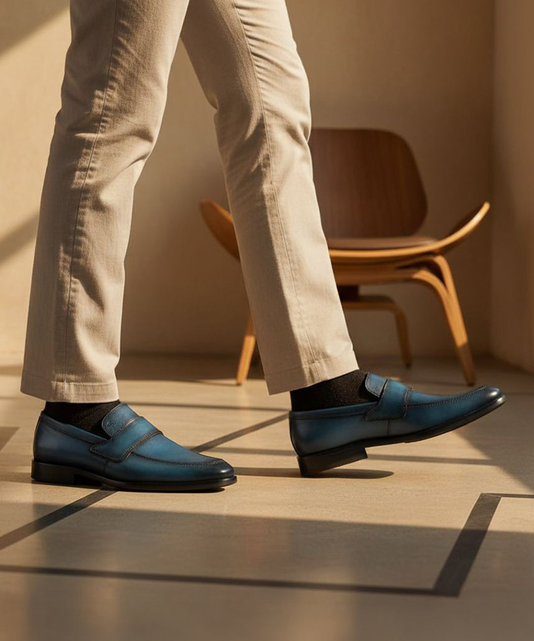 bugatti dark blue leather slip-on shoes with black socks and tan trousers, next to a wooden chair.
