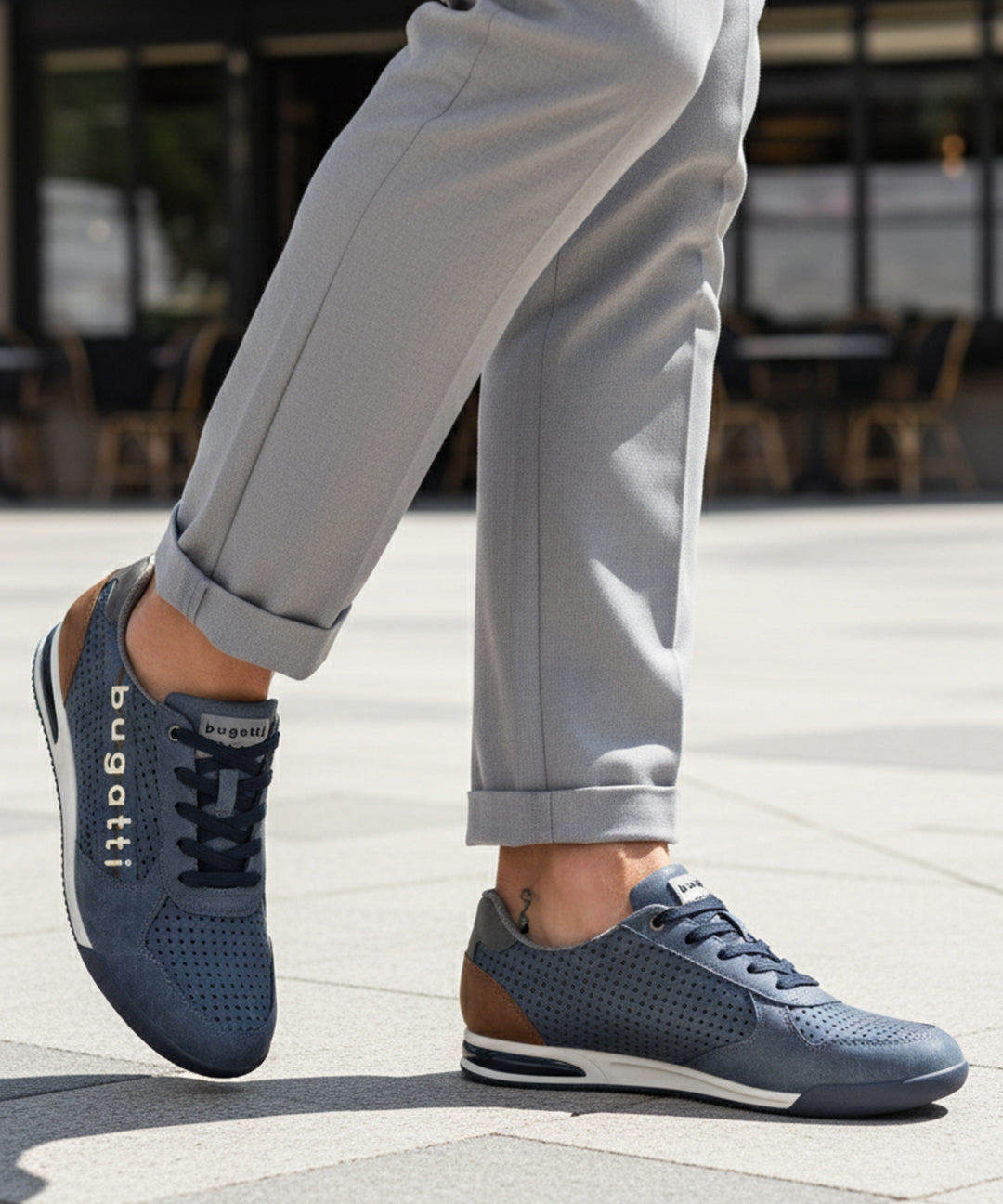 Lifestyle shot of bugatti Trevor blue Comfort Sneakers, a perforated leather shoe with brown heel detail, worn with gray slacks.
