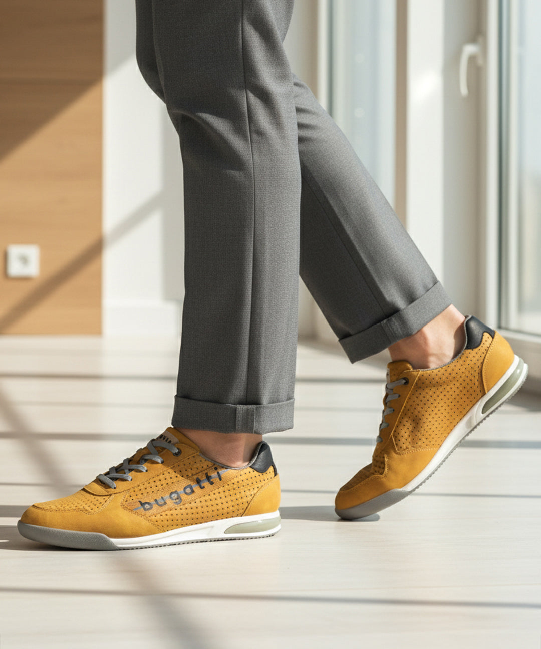 Lifestyle shot of bugatti Trevor yellow comfort sneakers, with grey laces, a perforated pattern, and grey dress pants.
