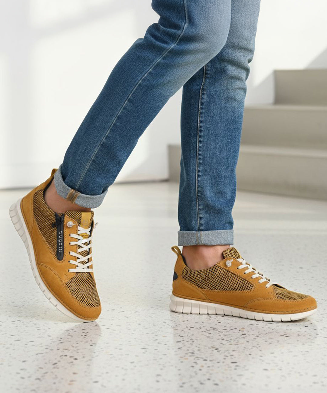 Lifestyle shot of bugatti Palenque yellow leather sneakers with white soles, worn with blue jeans.
