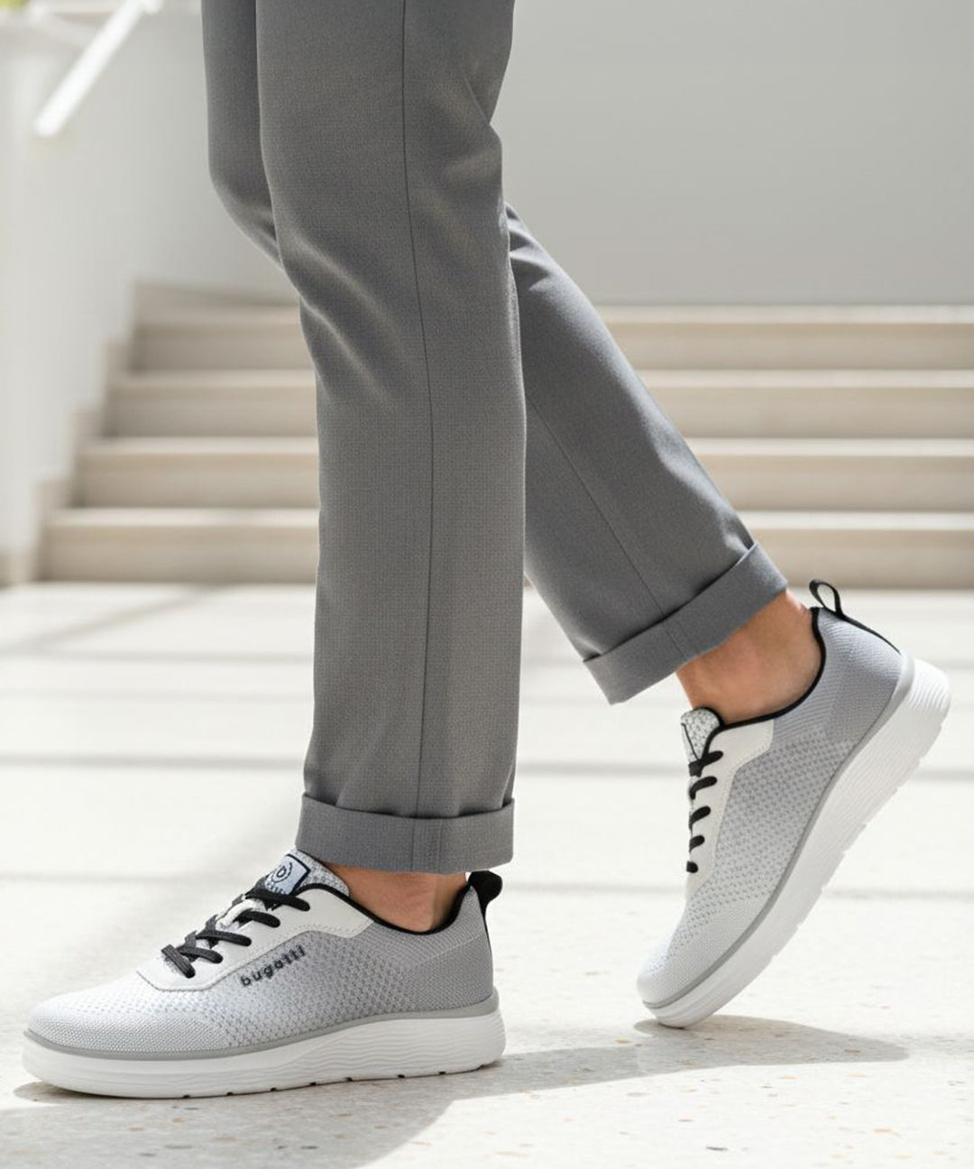 Lifestyle shot of bugatti Astra athleisure sneakers in white with black laces, paired with grey pants.
