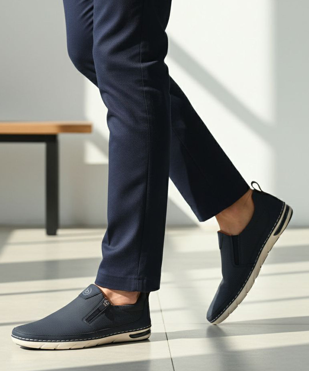 Lifestyle side view of bugatti Glenans dark blue slip-on shoes with zip detail, paired with dress pants.
