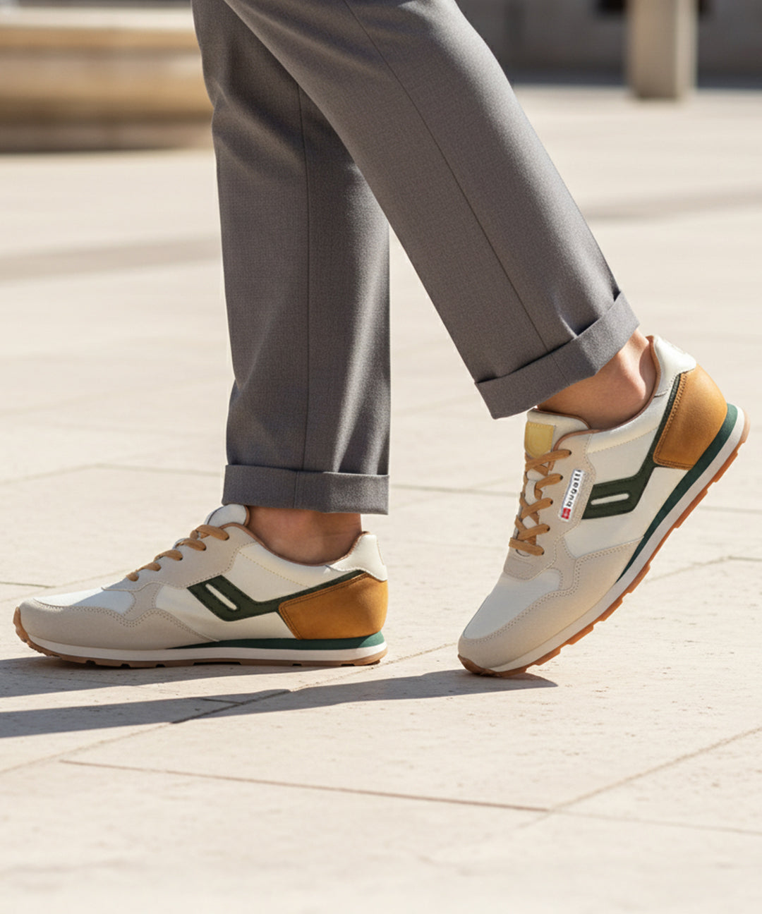 Lifestyle image of bugatti Sacramento offwhite comfort sneakers with green accents, brown heel, paired with gray dress pants.