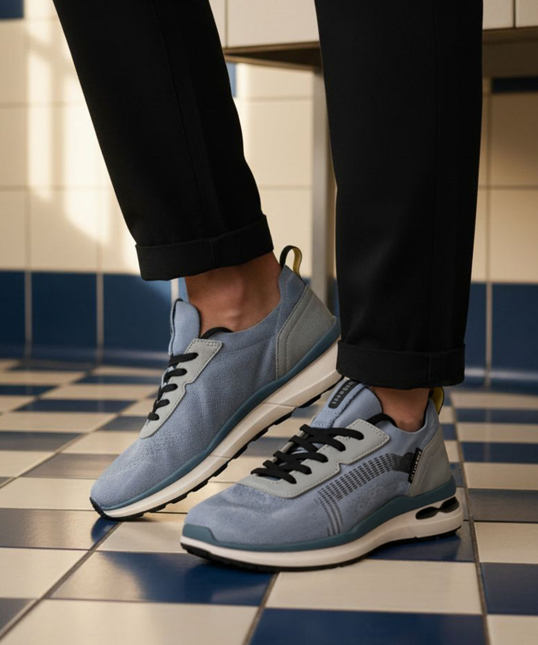 bugatti Sandar blue athleisure sneakers with black laces and white soles, paired with black cuffed pants.
