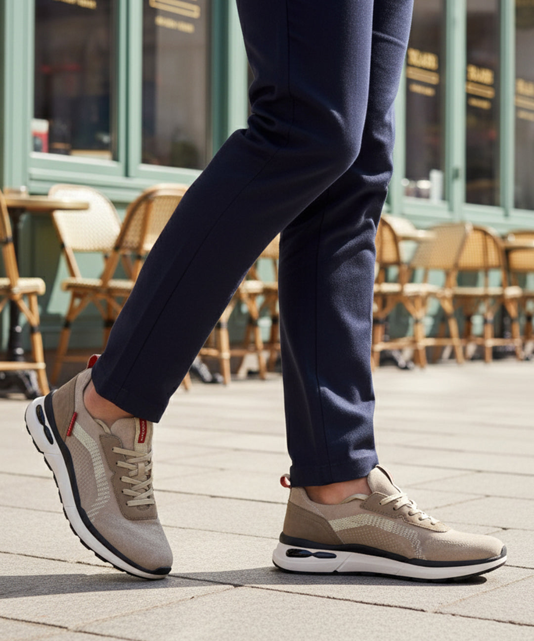Lifestyle cropped shot of bugatti Sandar beige athleisure sneakers, with white soles, worn with dark trousers.
