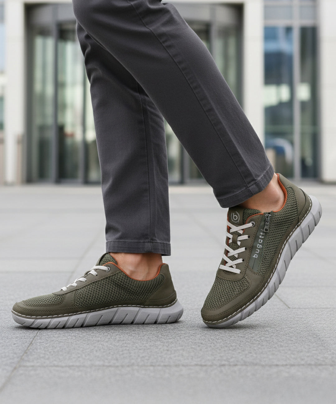 Cropped lifestyle view of bugatti Compton comfort sneakers in green, featuring a breathable mesh upper and white laces, worn with gray pants.
