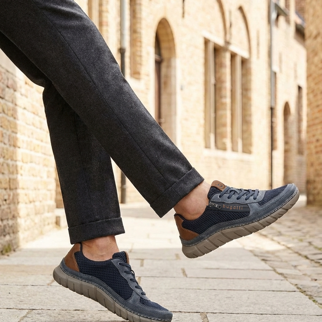 Lifestyle view of bugatti Compton dark blue comfort sneakers, with brown accent, worn with gray dress pants.
