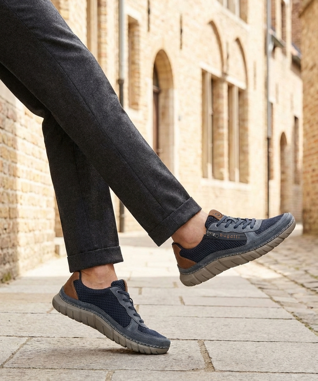 Lifestyle view of bugatti Compton dark blue comfort sneakers, with brown accent, worn with gray dress pants.
