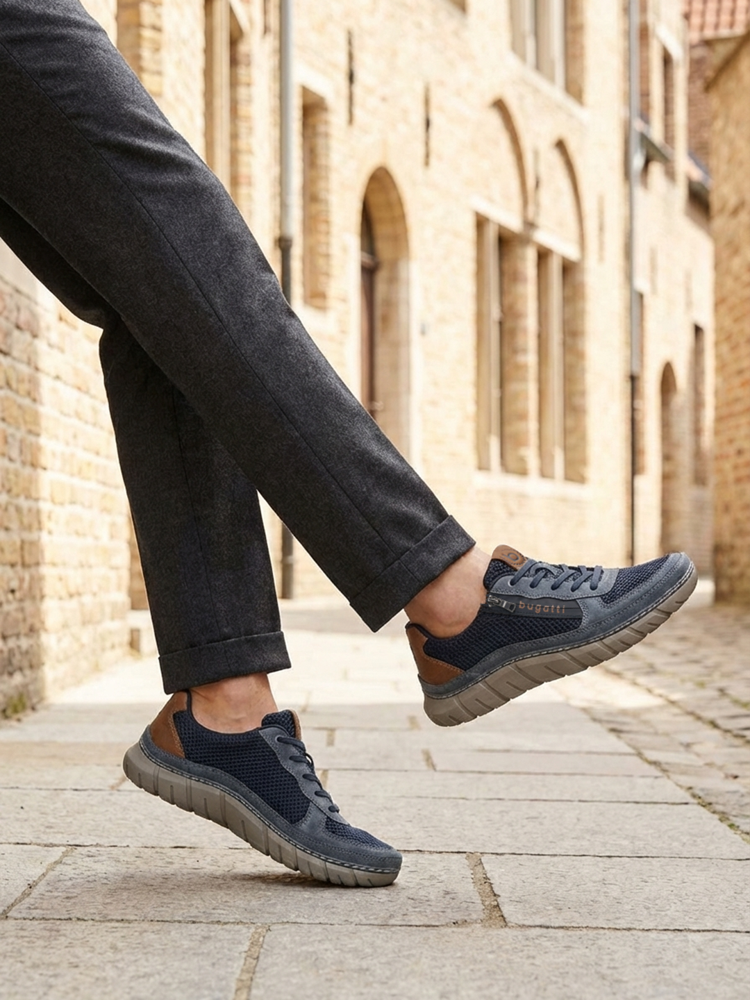 Lifestyle view of bugatti Compton dark blue comfort sneakers, with brown accent, worn with gray dress pants.
